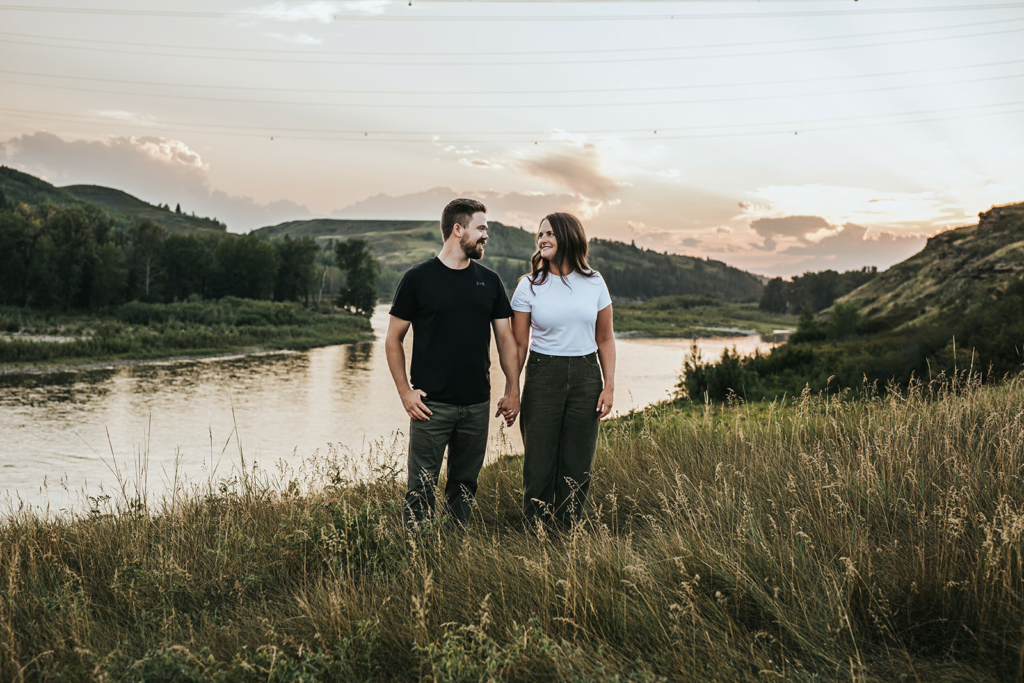 Couple holding hands during engagement photography session overlooking river