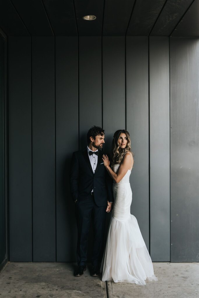 Bride and groom standing against dark wall as photographed by Calgary wedding photographer for modern couples Sue Moodie Photography